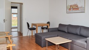 Een moderne woonkamer met een grijze modulaire bank, een houten eettafel met twee stoelen, en een klein houten bijzettafeltje.