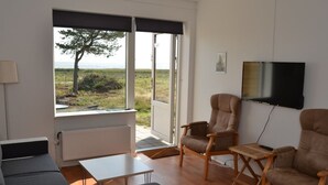 Ett vardagsrum med en soffa, fåtöljer, en tv och utsikt över omgivningarna.