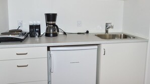Ett litet, praktiskt kök med en kaffebryggare, ett litet kylskåp och en diskho.