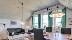 Een moderne woonkamer met een houten plafond, een eettafel met stoelen, een bank en een salontafel.