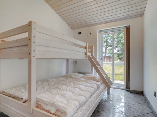A bunk bed room with a wooden frame, a window, and a tiled floor.