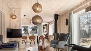 Moderni olohuone, jossa on puinen katto, litteänäyttöinen televisio, pyöreä sohvapöytä ja takka.