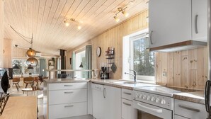 Moderni keittiö, jossa on valkoiset kaapit, ruostumattomasta teräksestä valmistettu uuni ja ikkuna, josta avautuu näkymä puita kohden.