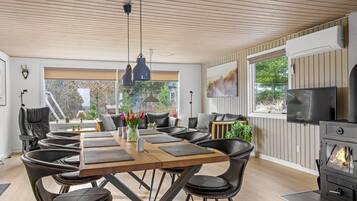 Un espace de salle à manger moderne avec une table en bois, des chaises en cuir noir, des luminaires suspendus et une cheminée.