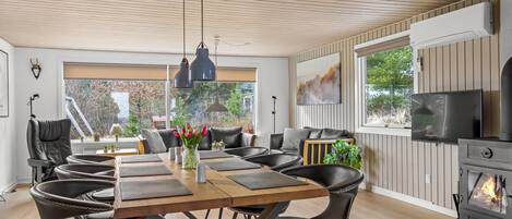 A modern dining area with a wooden table, black leather chairs, pendant lighting, and a fireplace.