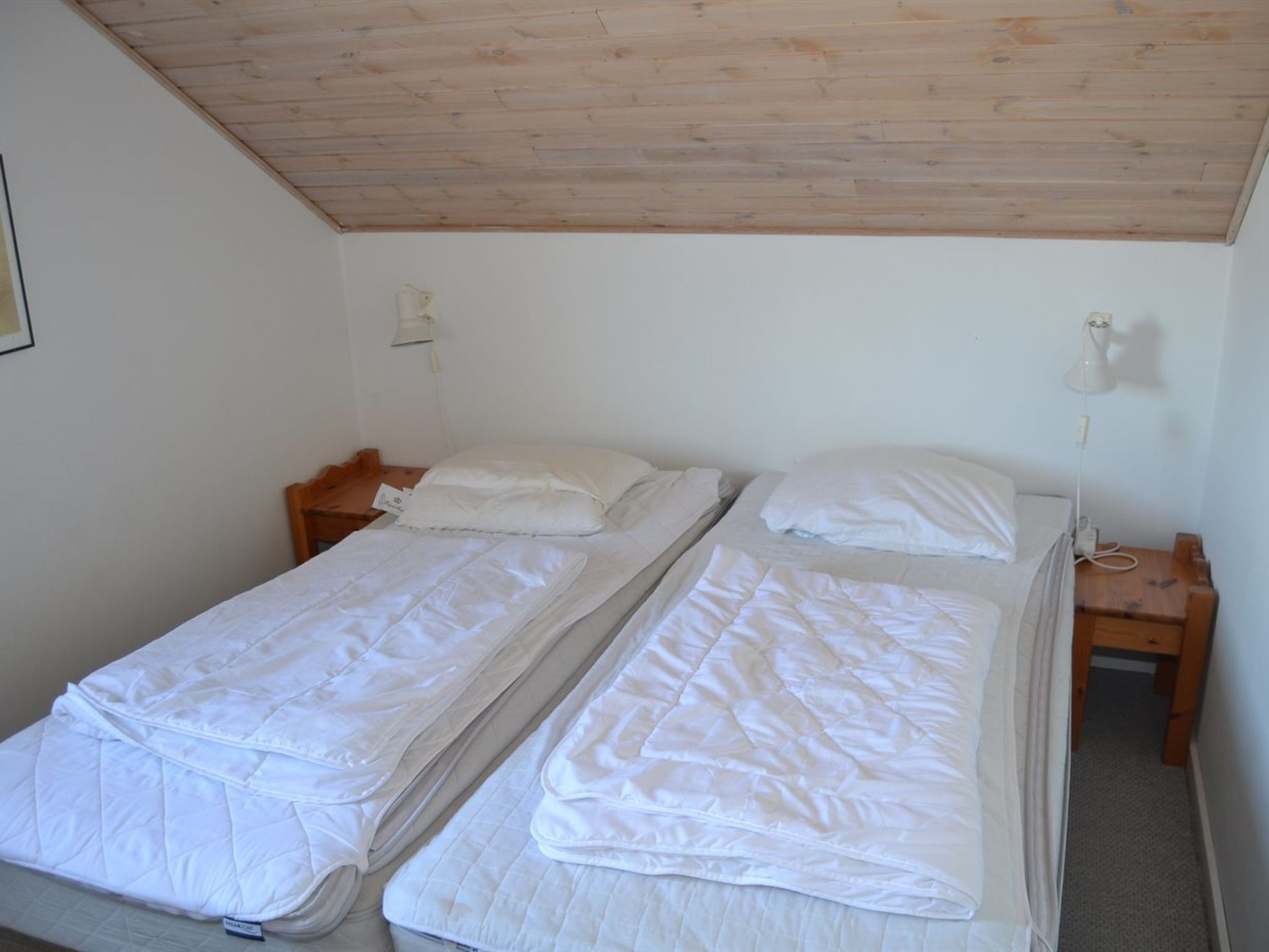 A room with two single beds, wooden headboards, a wooden ceiling, and a small bedside table with a lamp.