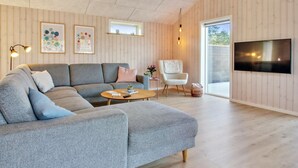 A modern living room with a grey sectional sofa, a wooden coffee table, a white armchair, and a flat-screen TV mounted on the wall.