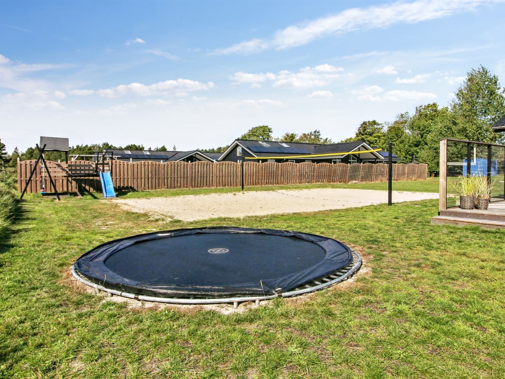 A backyard with a trampoline, a wooden fence, and a play structure.