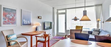 A modern hotel room with a dining area, a sofa, and a TV.