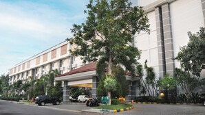 A multi-story hotel with a covered entrance, parked cars, and lush landscaping. - Lorin Dwangsa Solo Hotel (Surakarta)