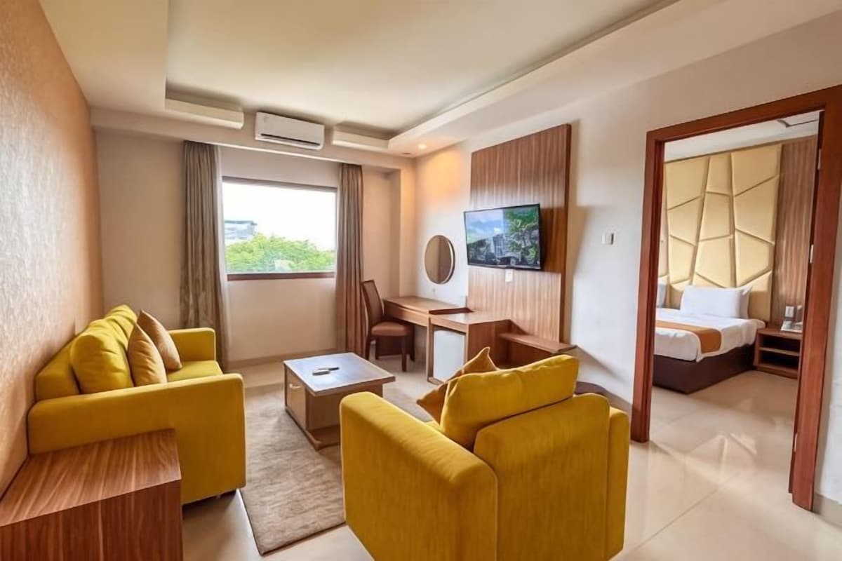 A hotel room with a seating area, a desk, a television, and a bed.