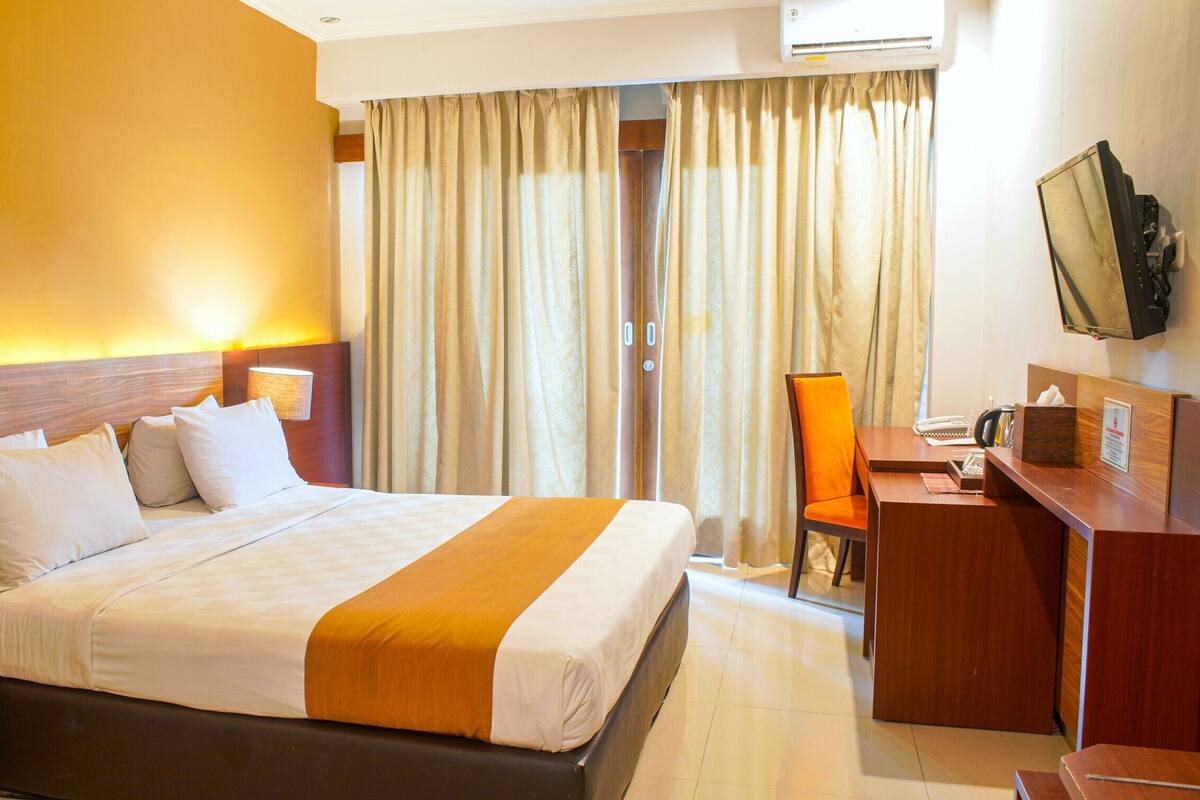 Une chambre d’hôtel avec un grand lit, un bureau, une chaise et un téléviseur fixé au mur.