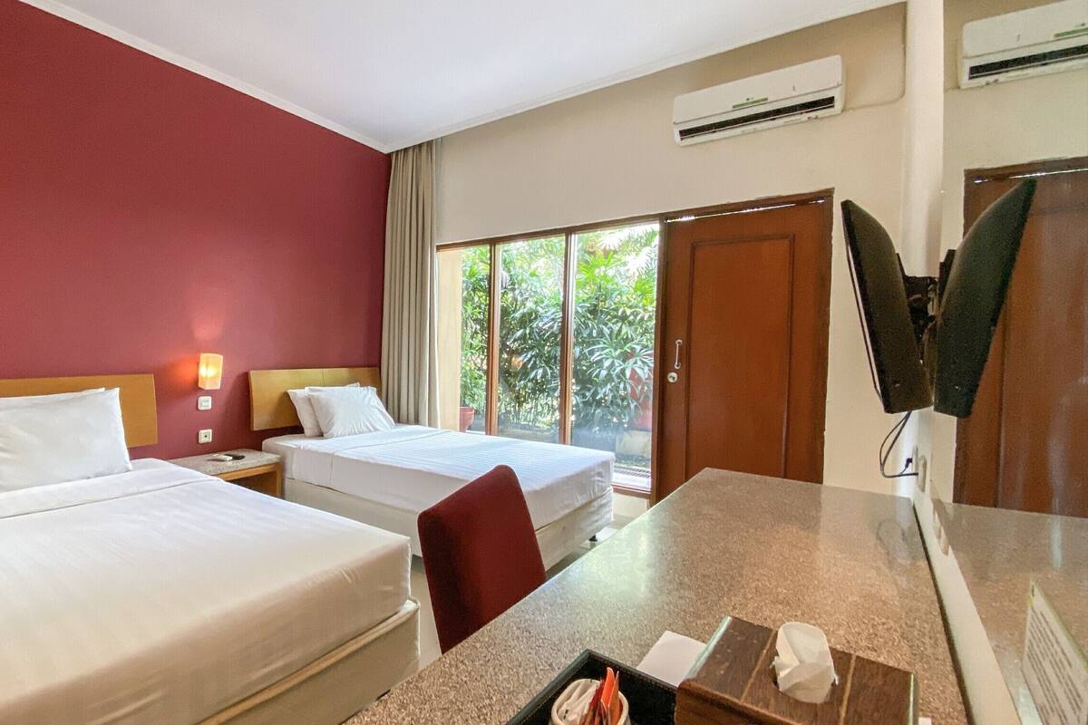 Une chambre d’hôtel avec deux lits, un bureau, une télévision et une fenêtre donnant sur un paysage verdoyant.