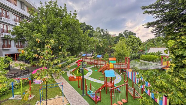 A playground with various play structures, surrounded by greenery and a building in the background. - Lorin Dwangsa Solo Hotel (Surakarta)