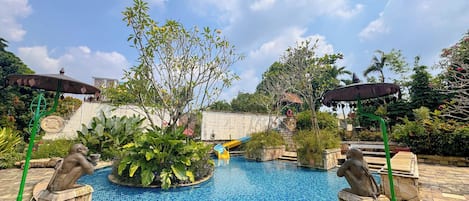 Una piscina con tobogán, rodeada de vegetación y estatuas de piedra.