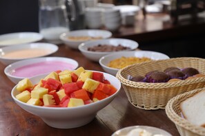 Une table de buffet proposant une variété d’aliments, notamment des saladiers de fruits, des pâtisseries et d’autres plats.