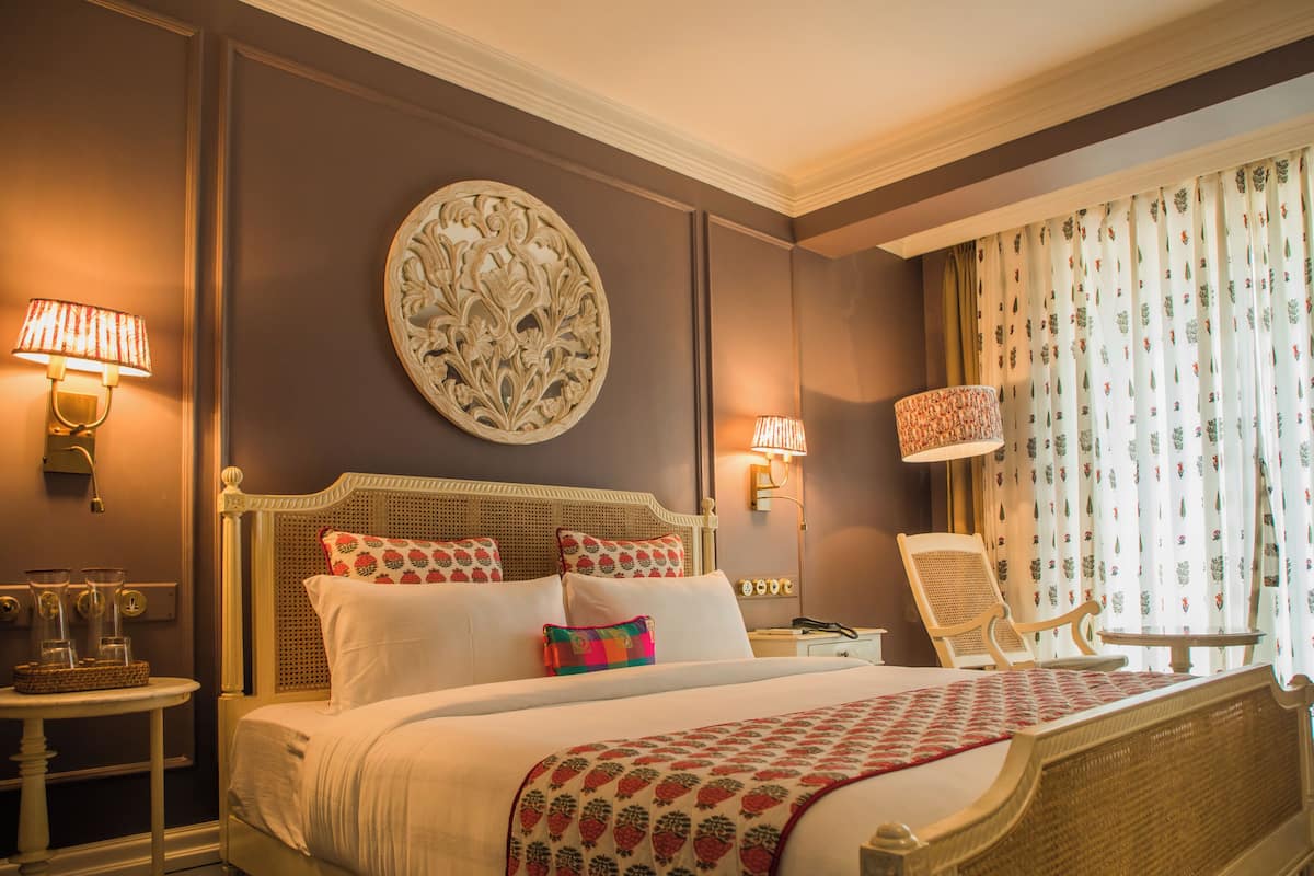 Habitación de hotel ordenada con una cama grande, dos mesitas de noche, una silla y un adorno en la pared.