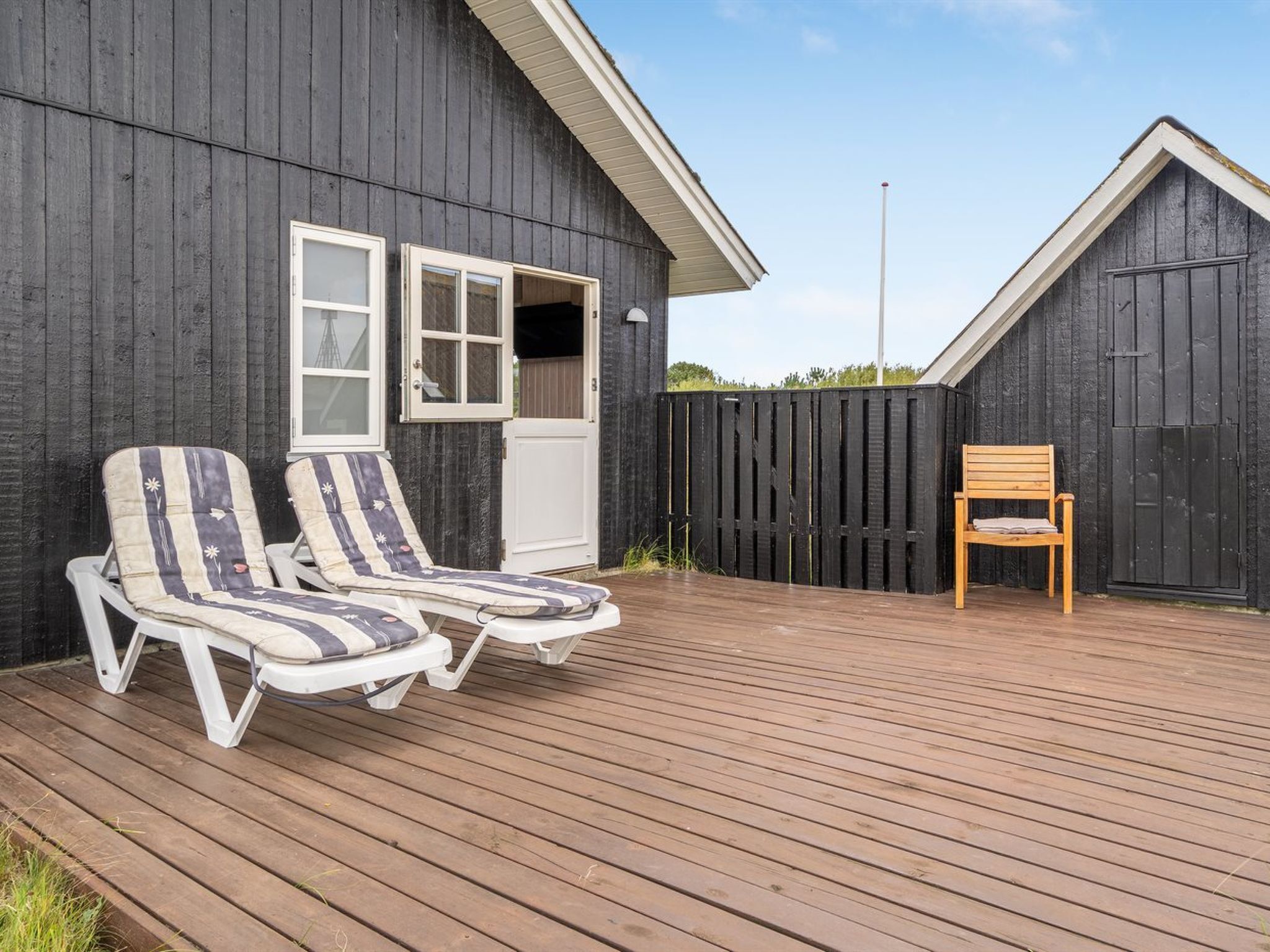 Eine Holzterrasse mit zwei Liegestühlen und einem Holzstuhl.