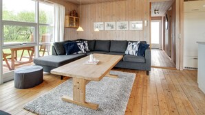 A modern living room with a wooden ceiling, a grey sectional sofa, a wooden coffee table, and a large window offering a view of greenery. - "Allis" - 400m from the sea by Interhome (Fanø)