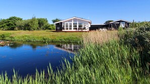 A modern house with a large glass window area, a pond, and surrounding greenery. - "Allis" - 400m from the sea by Interhome (Fanø)