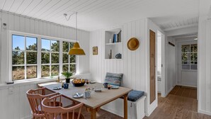 A dining area with a wooden table and chairs, a yellow pendant light, and a view of the outdoors through large windows. - "Neija" - 800m from the sea by Interhome (Fanø)