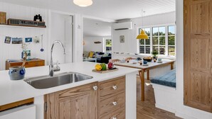 A modern kitchen with a central island, a sink, and wooden cabinetry. There is a dining area with a bench and a view of the outdoors. - "Neija" - 800m from the sea by Interhome (Fanø)
