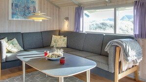 Et hyggeligt værelse med en grå sofa, et lille bord med en skål og to røde kopper, en seng med et tæppe, og et maleri af sejlbåde på væggen.