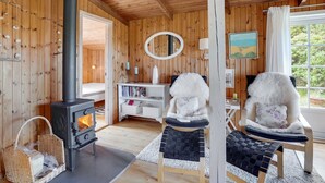 A cozy room with a wood-burning stove, two chairs with fluffy cushions, a white console table with books, and a large window with a view of greenery. - "Stefana" - 200m from the sea by Interhome (Fanø)