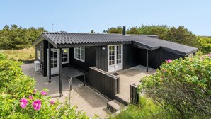 A small, dark wooden house with a tiled roof, a porch, and a garden with pink flowers. - "Stefana" - 200m from the sea by Interhome (Fanø)