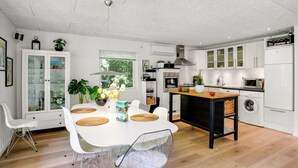 Eine moderne Küche mit wei ßen Schränken, einer zentralen Kochinsel und einem Essbereich mit weißem Tisch und Stühlen.
