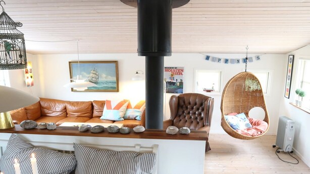 Un salon chaleureux avec un canapé en cuir, un fauteuil suspendu et une grande colonne noire.
