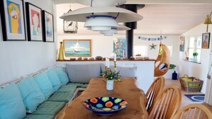 Un coin repas avec une table en bois, un saladier coloré et une vue sur la mer par la fenêtre.