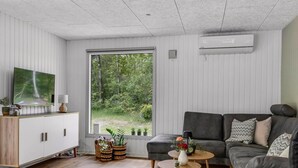 A modern living room with a sofa, a coffee table, a TV on a cabinet, and a large window with a view of greenery. - "Nyalle" - 30km from the sea by Interhome (Toftlund)