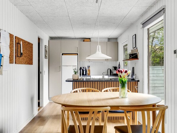 A modern kitchen with a central island, wooden chairs, a round table, and a hanging light fixture.
