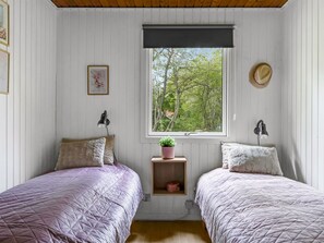 A bedroom with two beds, a window with a view of trees, a hat on the wall, and a small shelf with a plant.