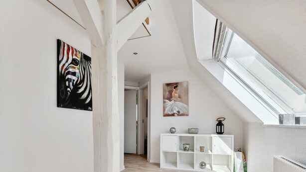 Um amplo loft com pé direito alto, piso de madeira, uma mesa consola branca e obras de arte nas paredes.