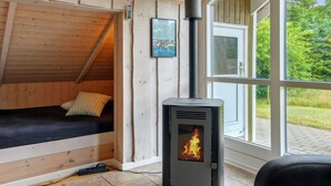 Een gezellige kamer met een bed, een houtkachel en een groot raam met uitzicht op groen.