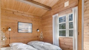 Ein Zimmer in einer Holzhütte mit einem Bett, zwei Nachttischlampen, einem Fenster und einem Bild an der Wand.