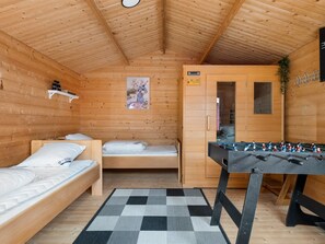 A wooden cabin with two beds, a foosball table, and a wardrobe.