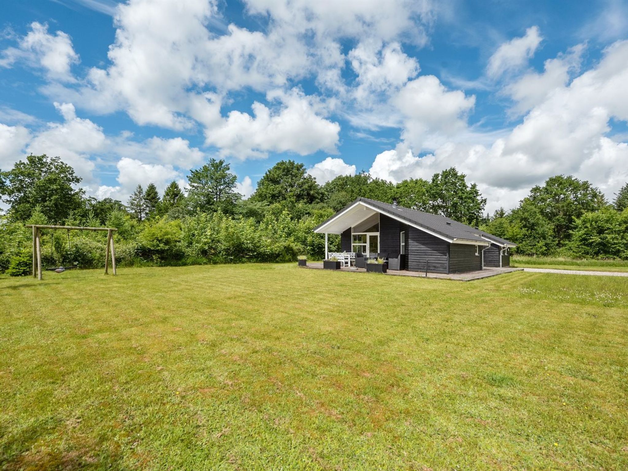 A single-story building with a porch and a covered patio area, surrounded by a grassy field and trees.