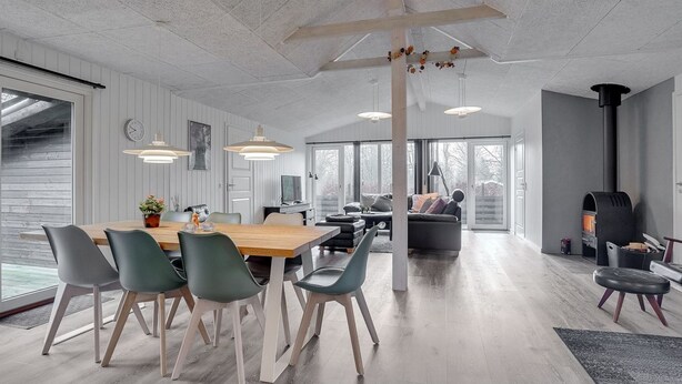 Een moderne woonkamer met een houten eettafel, groene stoelen, een bank en een open haard.