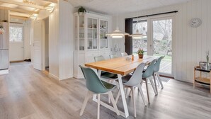 Een eethoek met een houten tafel, vier stoelen, een kast met glazen deuren en uitzicht op de omgeving door een groot raam.