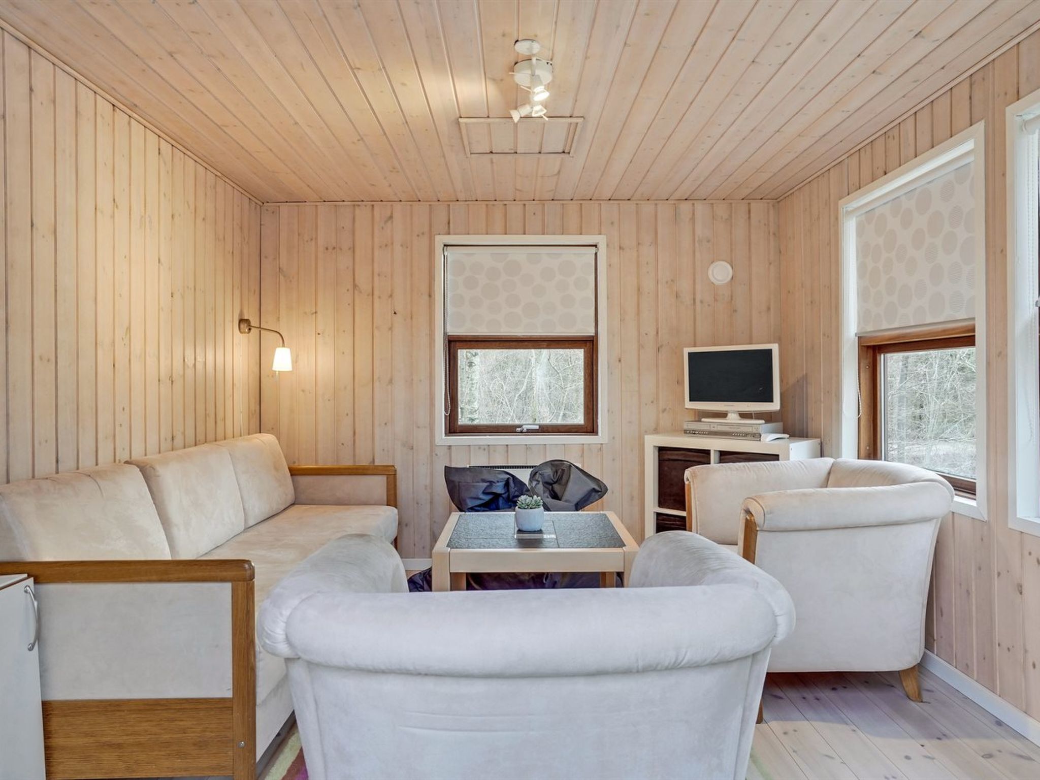 L’intérieur d’un chalet accueillant, avec des murs en bois, un canapé, un fauteuil, une petite table et un téléviseur.