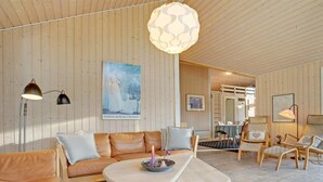 A modern interior with a wooden ceiling, a round table with a candle, leather sofas, and a dining area with chairs.