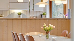 A dining area with a table set for four, a vase with flowers, and pendant lights above.