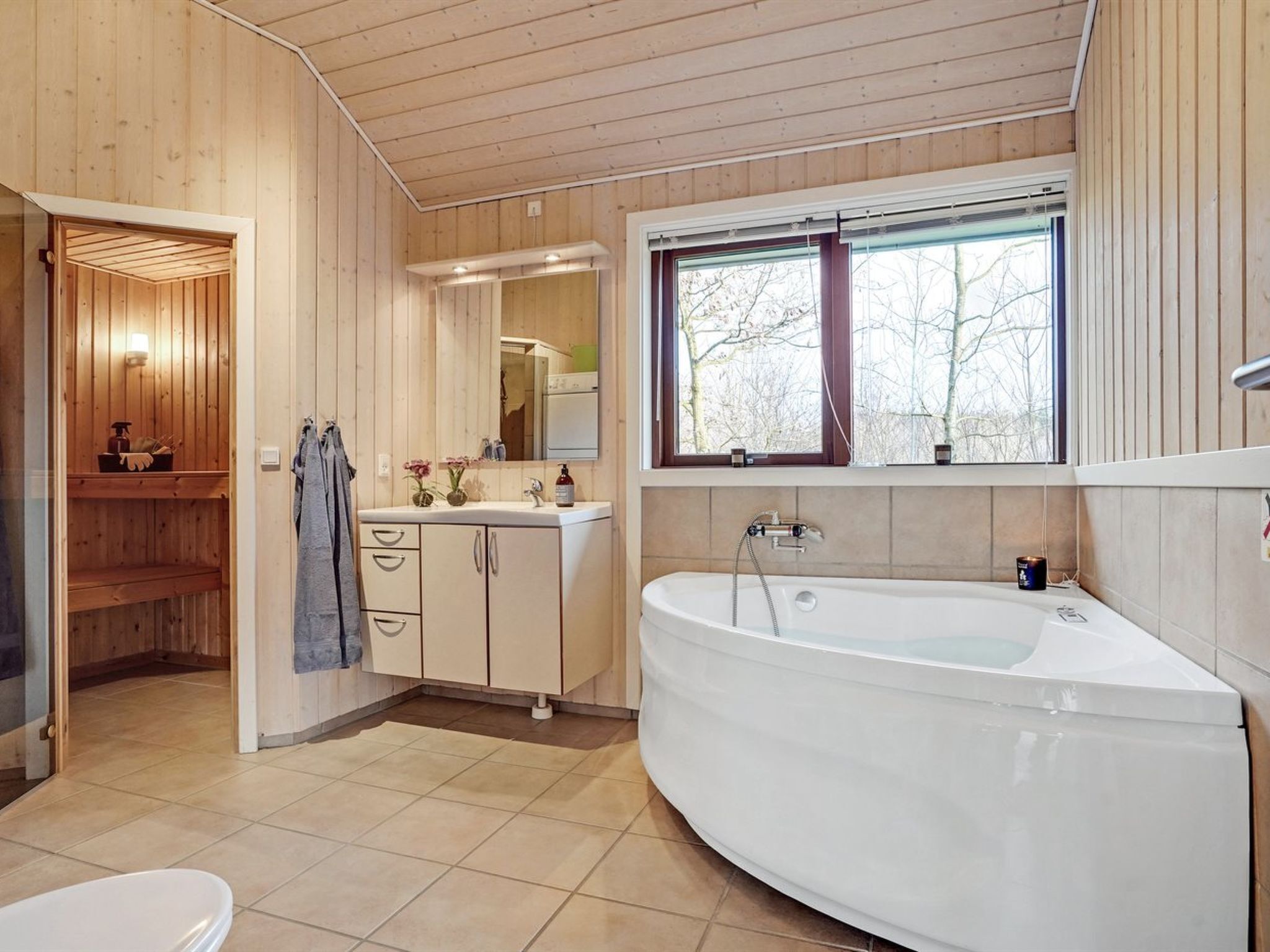 Un baño moderno con una bañera independiente, un espejo grande y un ventanal con vistas a árboles.