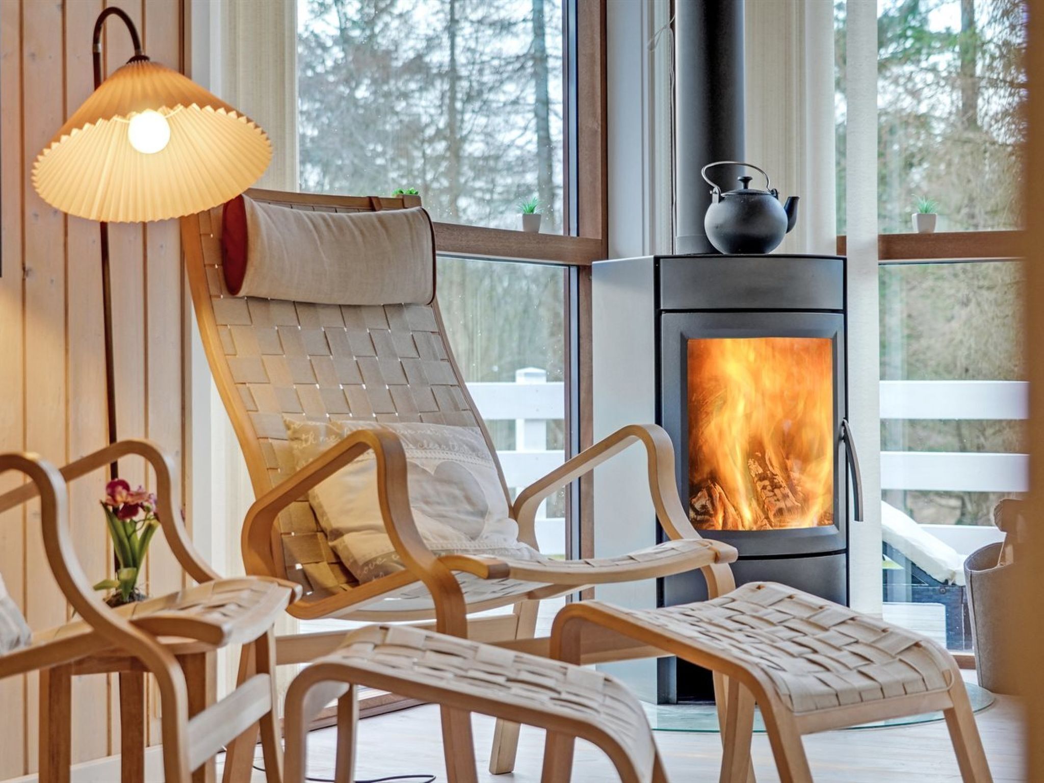 Une pièce chaleureuse avec une cheminée, des fauteuils en osier et une lampe suspendue.