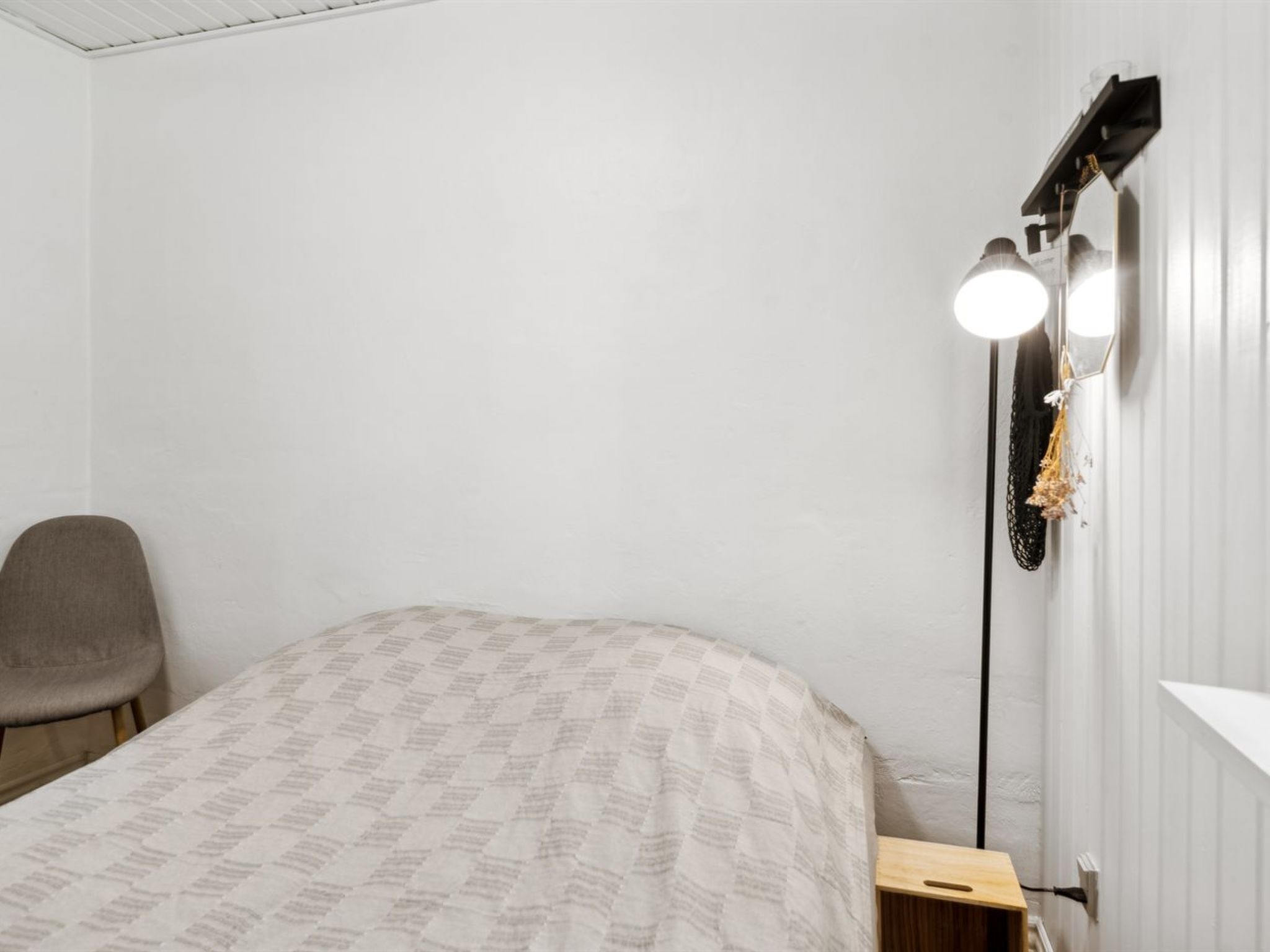 Een slaapkamer met een bed, een stoel, een nachtkastje en een wandlamp.