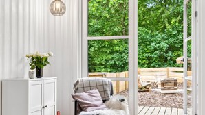 A room with a white cabinet, a chair with a plaid blanket, and a view of a wooden deck and greenery outside. - "Helghi" - 30km from the sea by Interhome (Toftlund)