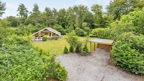 A yellow cabin with a porch, surrounded by dense greenery and trees.